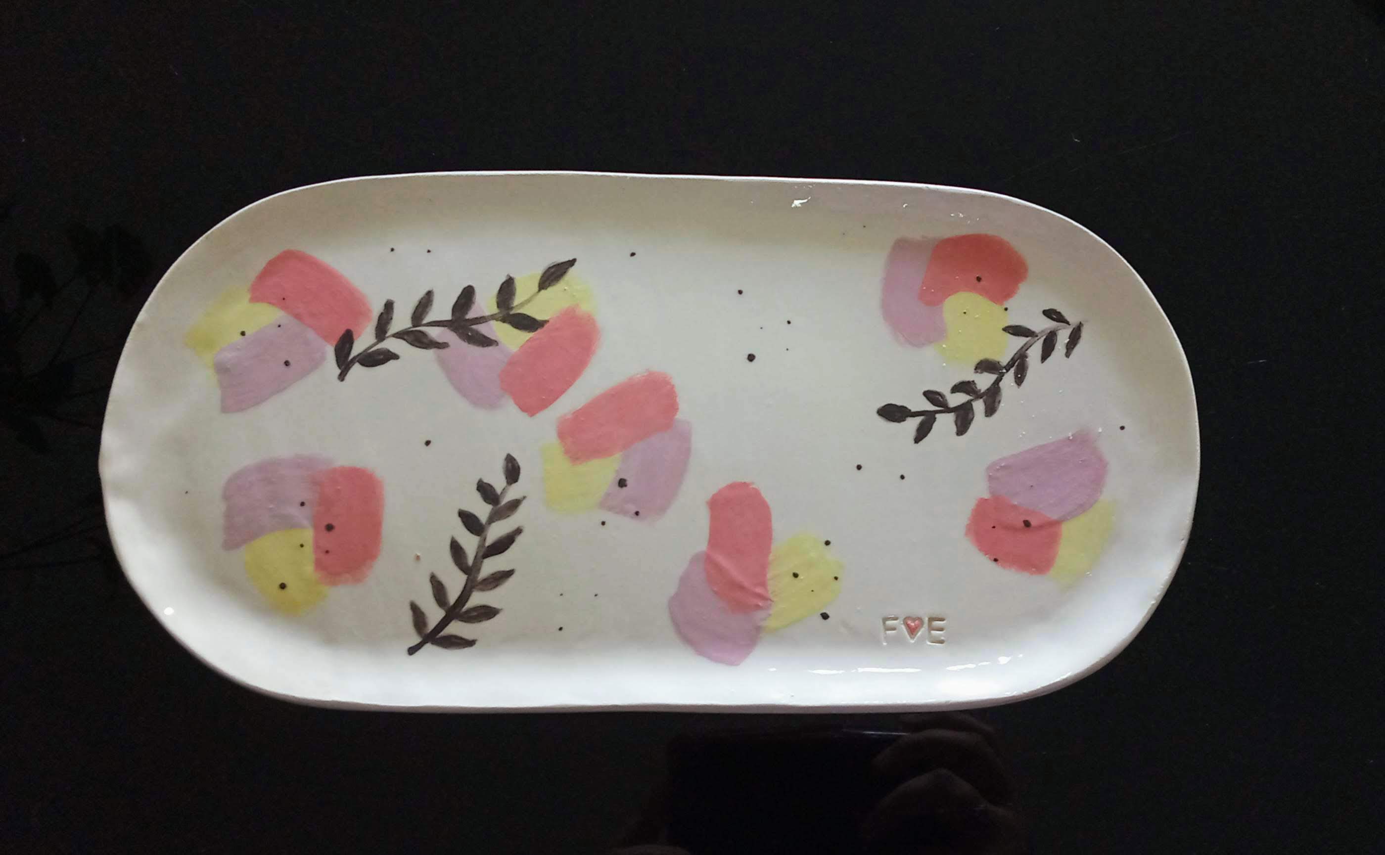 bandeja mediana de forma ovoide, de fono color hueso y decoración con engobe negro en forma de hojas pequeñas y manchas de colores amarillo, lila y coral pastel